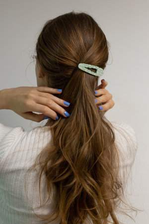 Beautiful long blond natural hair with flower hair clip snap view from the back against white background. Caucasian woman with purple nails.の写真素材