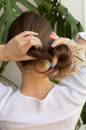 Woman making hairstyle with her hands with purple nails against white background and monstera plant. Photo in movement. Young caucasian woman.の写真素材