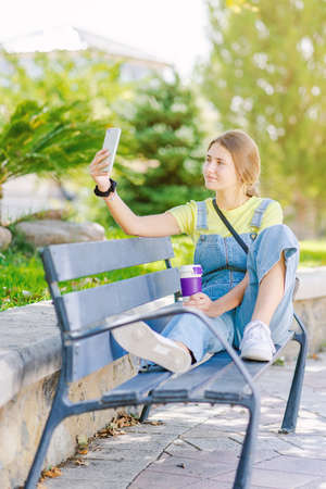 Young woman takes coffee in the park, relaxing, while having her picture taken. Lifestyle, happiness, woman.の写真素材