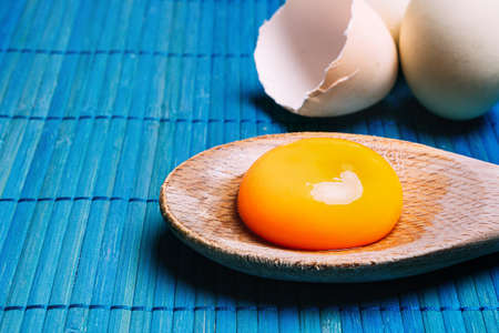 Raw egg yolk in a spoon next to eggs, on a blue background Ecological, traditional and healthy cookingの写真素材