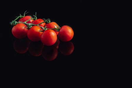 Cluster of cherry tomatoes on a black background Fresh and organic tomatoes. Reflectionの写真素材