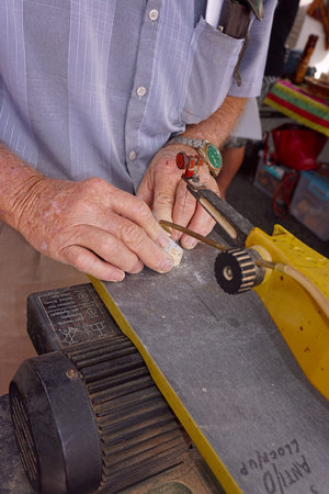 The hands of an old man using a powered fretsaw machine to make small wooden toys.