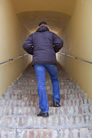 Young successful man walking upstairs to reach light at the end of tunnel.の写真素材