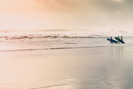Surfers running on the beach at sunset.の写真素材