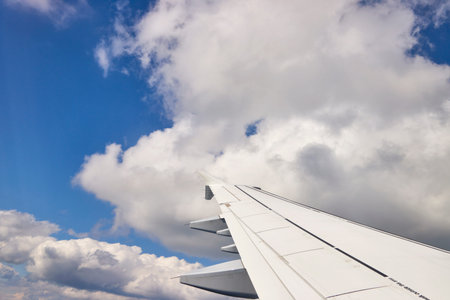 Wing of an airplane flying in the blue sky with white clouds.