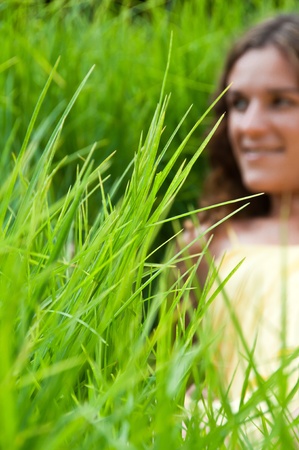 Girl in long green grass field with focus set on front grasses の写真素材