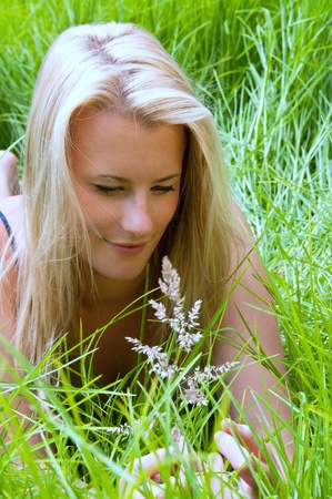 Blonde girl studying grass seed head in meadow while relaxing in the sunshineの写真素材