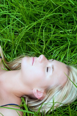 Blonde beauty resting in a field of long fresh green grass during summerの写真素材