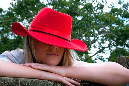 Blonde girl leaning on fence with red stetson style hat on at a farmの写真素材