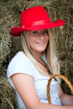Country girl sitting in the haybarn with a red stetson style hatの写真素材