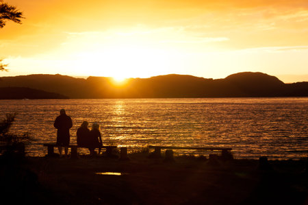 Family in silhouette watching sunset over lake