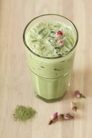 glass of green tea latte decorated with dried rose on wooden backgroundの写真素材