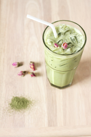 glass of green tea latte decorated with dried rose on wooden backgroundの写真素材