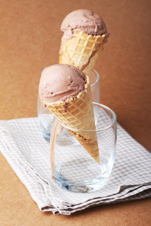 couple of chocolate flavor ice cream cones in a glass on matte texture brown backgroundの写真素材