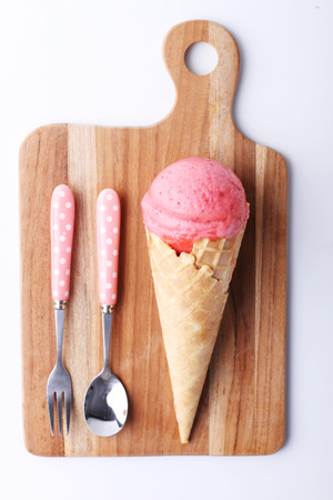 red strawberry ice cream cone with spoon on wooden plate on white backgroundの写真素材
