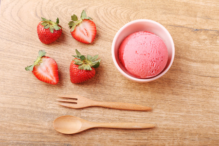 red homemade strawberry ice cream scoop with fresh strawberry on wooden plate on wooden backgroundの写真素材