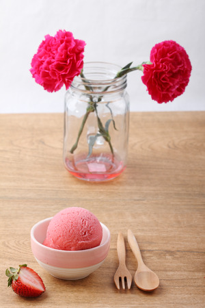 red homemade strawberry ice cream scoop with fresh strawberry on wooden plate on wooden backgroundの写真素材