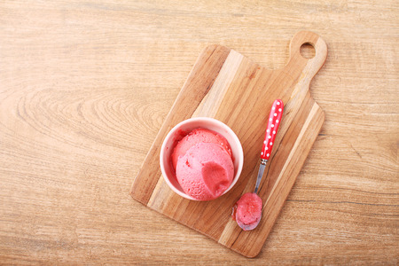red homemade strawberry ice cream scoop with spoon on wooden plate on wooden backgroundの写真素材