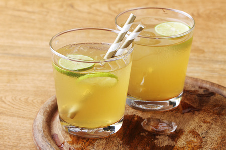 cold gold soft drink from lime and honey with gold straw on wooden boardの写真素材