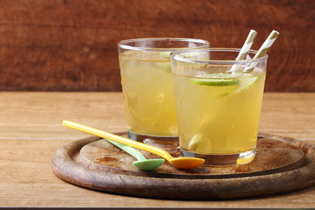 cold gold soft drink from lime and honey with gold straw on wooden boardの写真素材