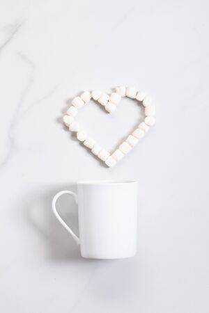 White ceramic cup of hot cocoa on top of white marble background with heart shape marshmallowの写真素材