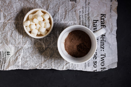 White ceramic cups of hot cocoa with marshmallows on top of rustic black background