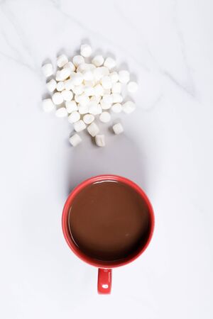 Red ceramic cups of hot cocoa with marshmallows on top of white marble backgroundの写真素材