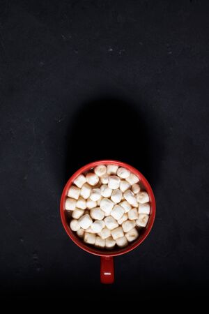 Red ceramic cups of hot cocoa with marshmallows on top of black rustic backgroundの写真素材