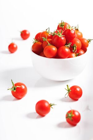 red cherry tomato in white ceramic bowl on white backgroundの写真素材