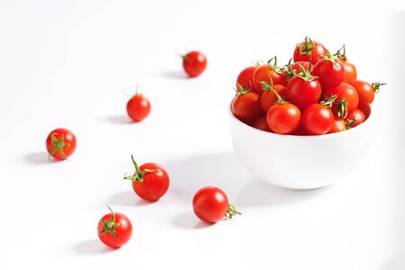 red cherry tomato in white ceramic bowl on white backgroundの写真素材