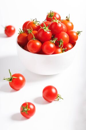 red cherry tomato in white ceramic bowl on white backgroundの写真素材