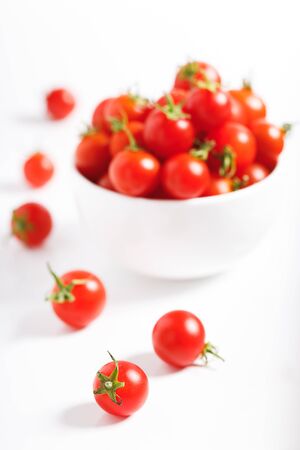 red cherry tomato in white ceramic bowl on white backgroundの写真素材
