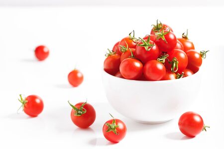 red cherry tomato in white ceramic bowl on white backgroundの写真素材
