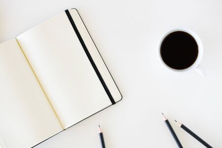 A cup of hot black coffee on white table background with notebook and stationery.  Work from home concept.の写真素材