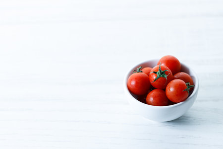 red cherry tomato in white ceramic bowl on white backgroundの写真素材