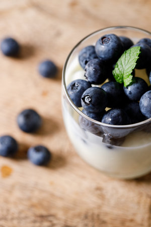 Ripe organic blueberries with yogurt in a glass on rustic wooden table background. Selective focus.の写真素材