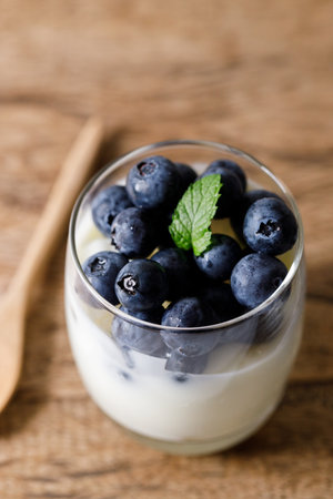 Ripe organic blueberries with yogurt in a glass on rustic wooden table background. Selective focus.の写真素材