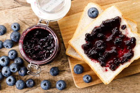 Blueberry jam with fresh berries on bread on rustic wooden table background. Selective focus.