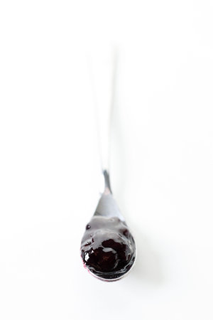 Spoon of blueberry jam on white marble table background. Selective focus.