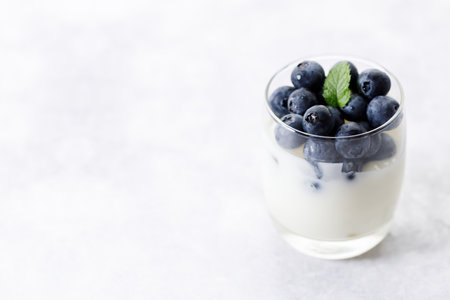 Ripe organic blueberries with yogurt in a glass on white stone table background. Selective focus.の写真素材