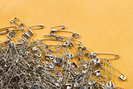 A number of stainless safety pins on brown paper background.