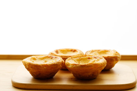 Stack of Portuguese sweet dessert egg tart or Pastel de Nata on wooden board on wooden table. ...