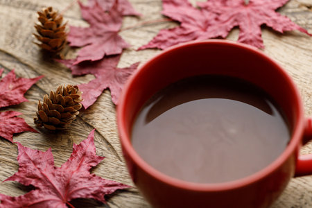 Cup of delicious hot chocolate with red maple leaf on wooden table background. Selective focus.の写真素材