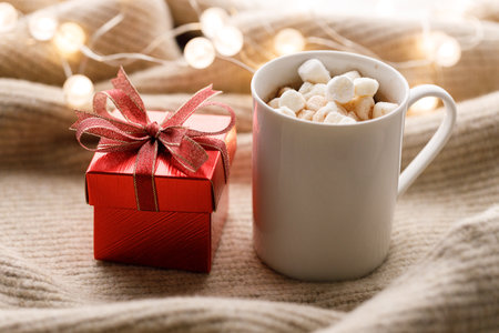 Cup of delicious hot chocolate and artisanal gift box tied with bows on warm sweater. Christmas New year concept. Selective focus.の写真素材