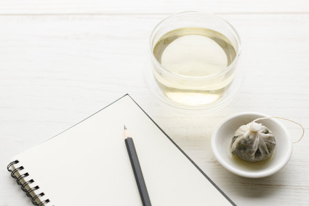 Cup of hot tea with tea bag and notebook with pencil on white wooden table. Study time. selective focus.の写真素材