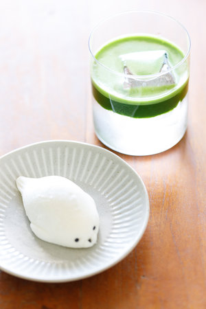 fresh matcha tea, green tea pouring on a glass of coconut water and daifuku Japanese confectionery on wooden table. Selective focus.の写真素材