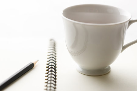 Cup of hot and notebook with pencil on white table background. Study time concept. selective focus.の写真素材
