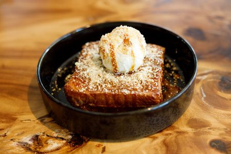 Fresh bread butter toast with Vanilla flavor ice cream on black ceramic plate on wooden table. Selective focus.の写真素材