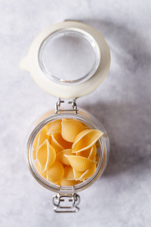 Raw uncooked dried Conchiglie shell pasta. Italian seashells pasta in lock lid jar on white...