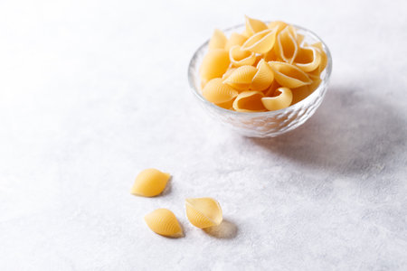 Raw uncooked dried Conchiglie shell pasta. Italian seashells pasta in glass bowl on white background. Selective focusの写真素材